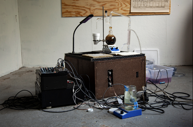 Image of a work of art entitled Redox Drip. A box with many wires, and beakers connected.