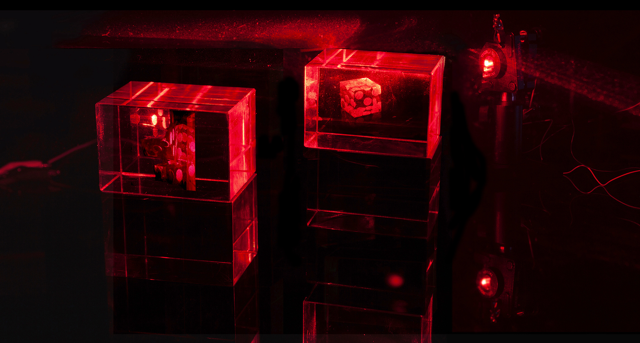 Two transparent cubes glow with red laser light in an ambiguous deep black surround. A holographic image on each mount depicts dice, which appear suspended in space and/or time. The vibe is a bit mysterious, maybe something like: "mystic makes a long shot in the dark".