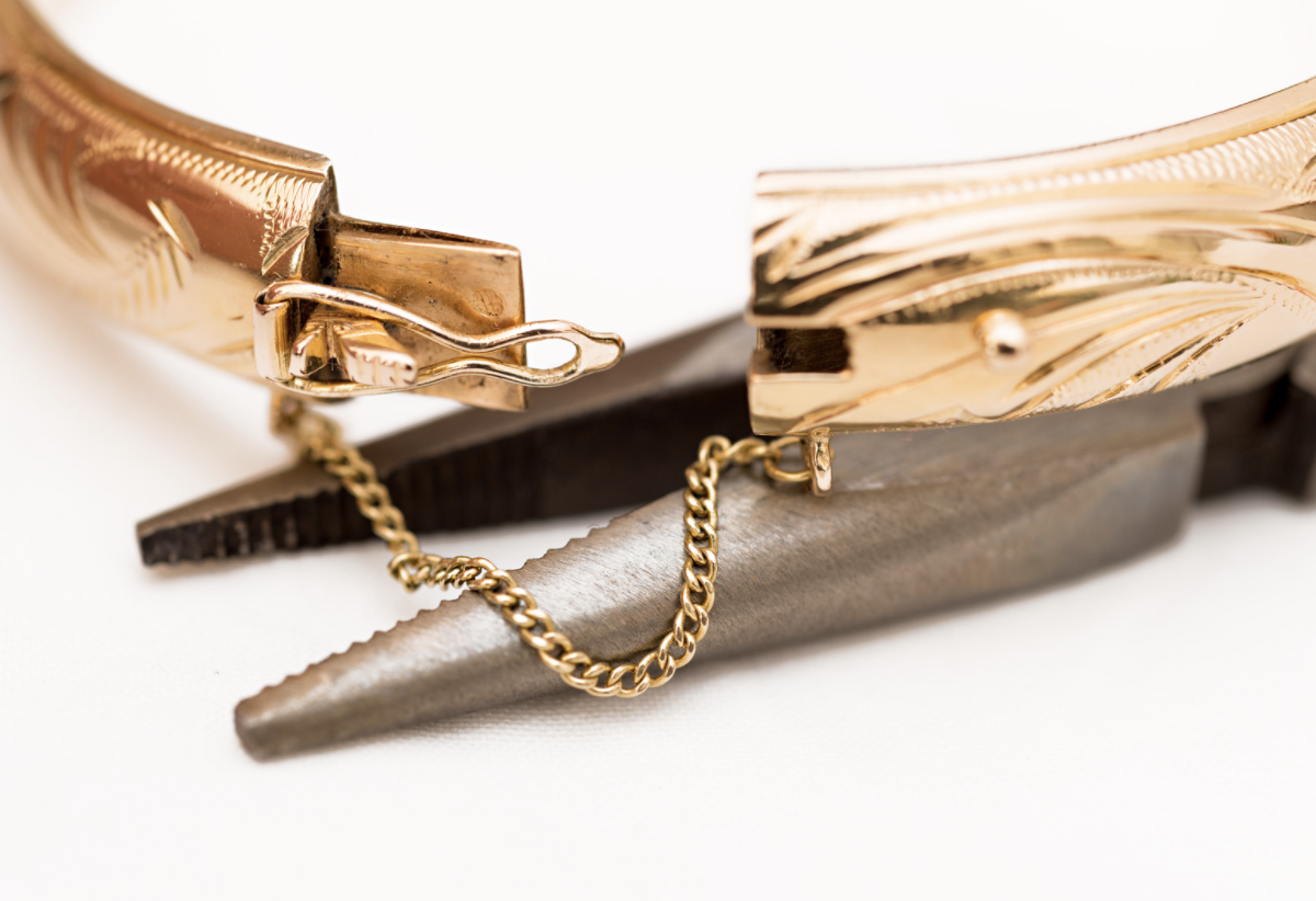 closeup image of a pair of pliers and a gold bracelet with the chain hanging over the wire