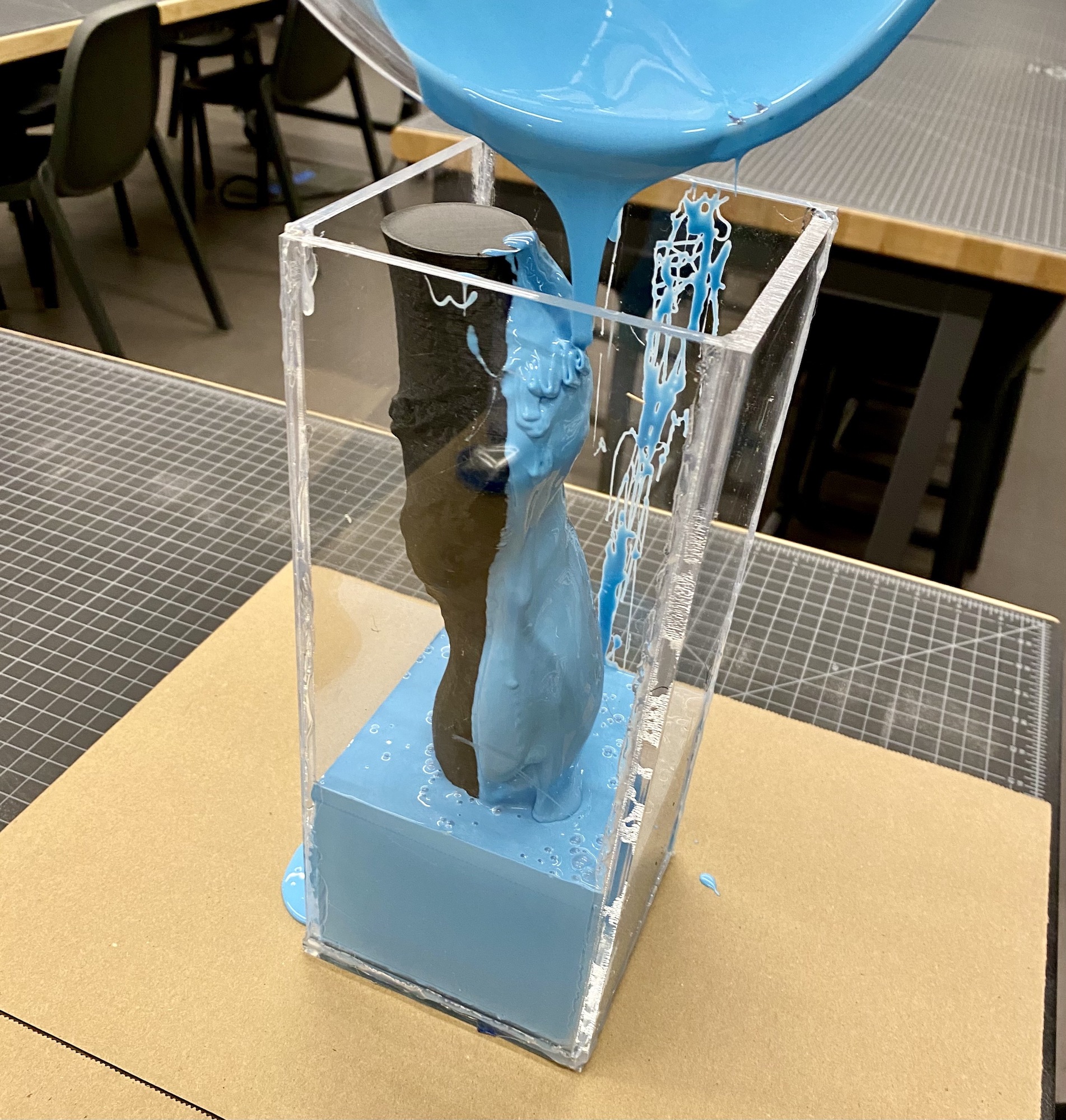 Blue silicone being poured into a box mold with a 3D printed tree trunk