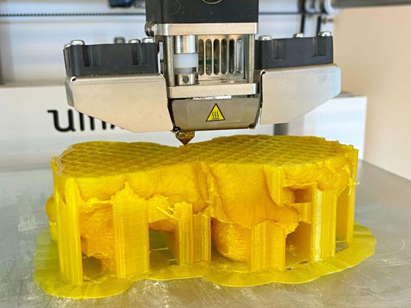 3D printer prints an object with yellow plastic filament