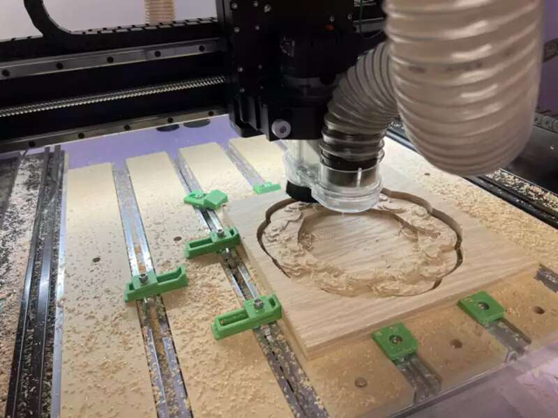 Close up photo of the bed of the CNC machine with a piece of wood that is halfway through carving.